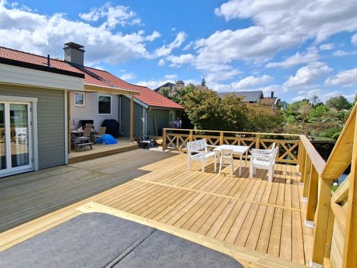 Altanbygge med nedsänkt SPA bad Uteplats med trädäck, stolar och vy över omgivande grönska och byggnader.