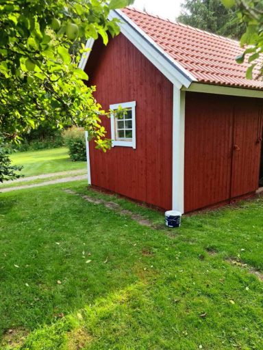 Hus målning Faluröd färg Litet röd träbyggnad med vit fönsterkarm i grönskande trädgård.